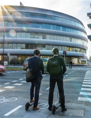 Two people waiting at a crossroads on e scooter