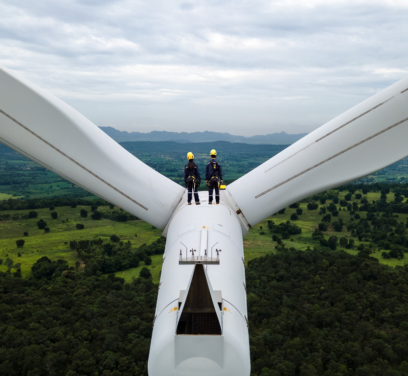 Two men standing on a wind turbine, looking at the environment of the towering structure.