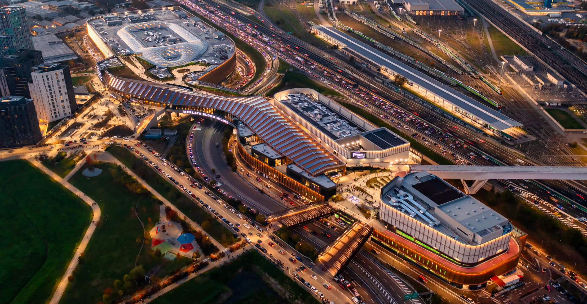 Overhead perspective of a cityscape showcasing a train station amidst a network of roads and buildings.