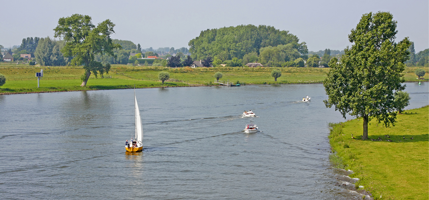 River de maas met bootjes op het water en dijken op achtergrond