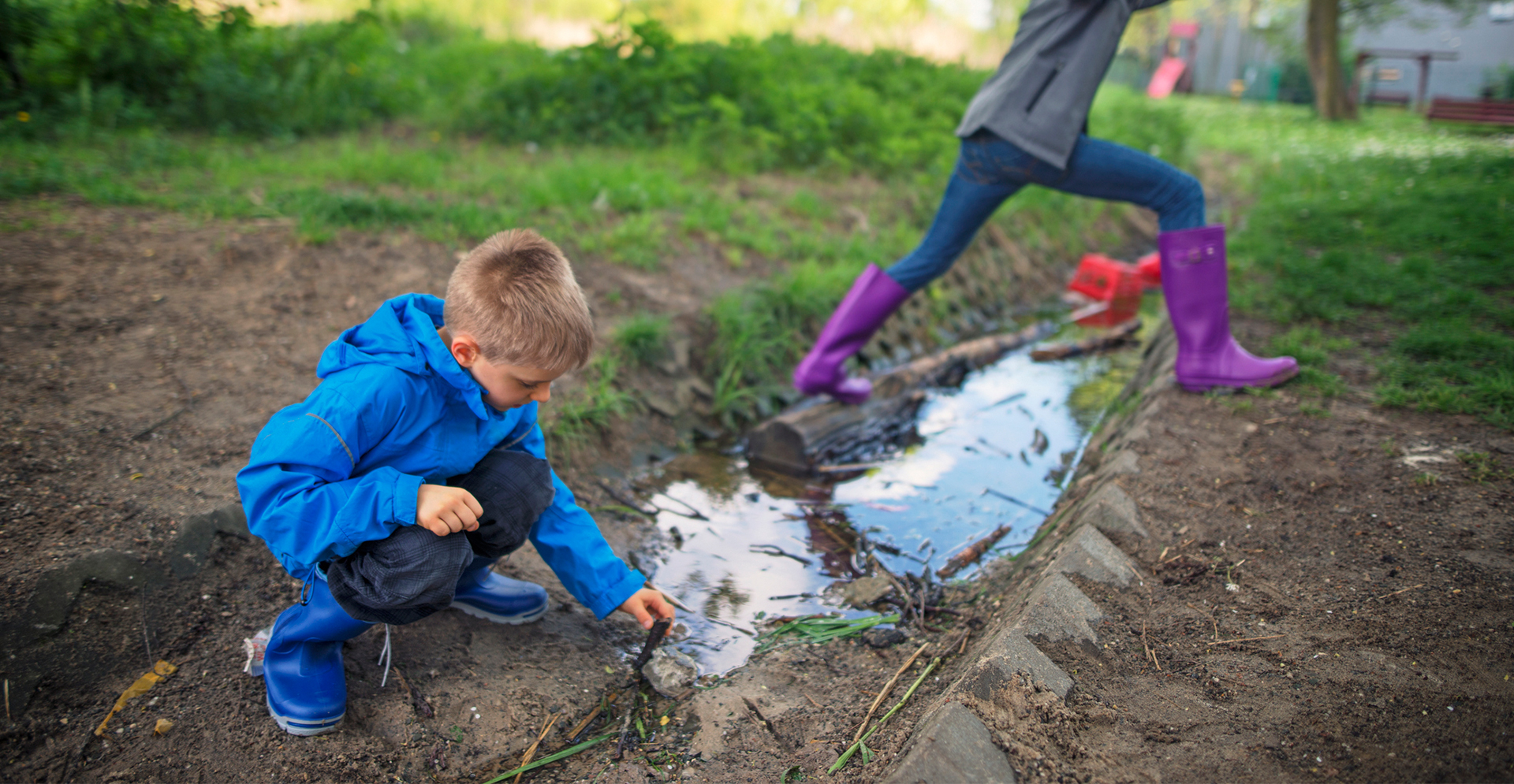 Kinderen met mogelijk PFAS houdende kleding (kunststof laarzen en regenkleding) spelen bij een sloot.