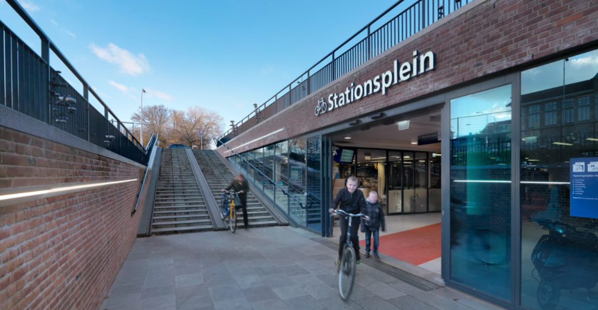 Jongen fietst weg uit de fietsenstalling bij station Deventer en andere reizigers komen net aan.